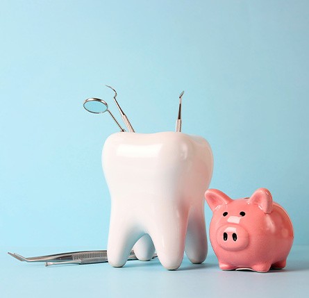 A pink piggy bank and tooth model next to dental instruments