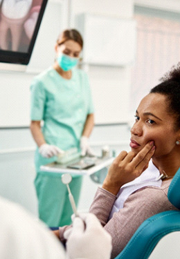 Woman in dental chair touching sore jaw to show dentist where it hurts
