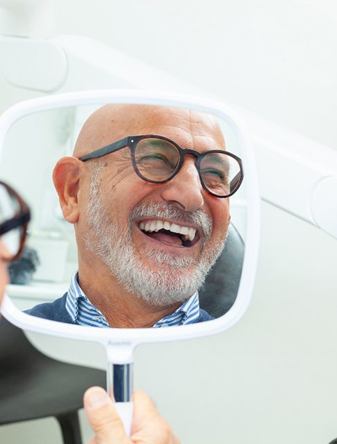 Man with black glasses smiling in reflection in mirror