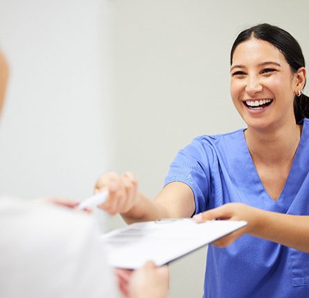 Smiling dental assistant handing patient forms