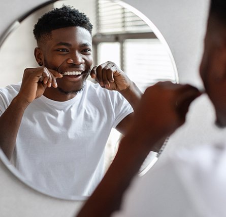 Man smiling while flossing in bathroom