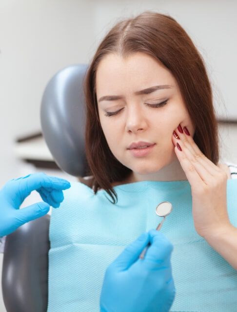 Woman in the dental chair holding her cheek in pain