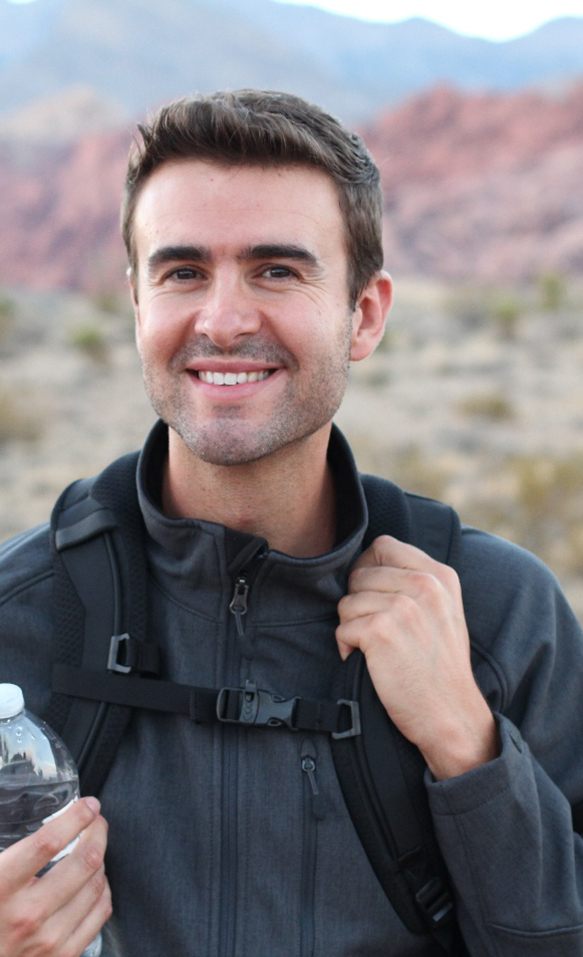 A young, smiling man hiking in an outdoor setting