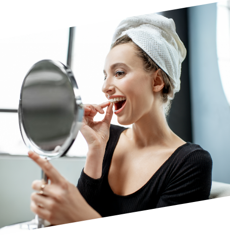 Woman holding a mirror and placing a whitening tray over her teeth
