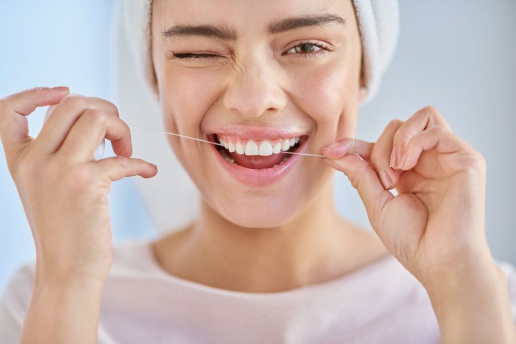 A woman flossing her teeth in the mirror.